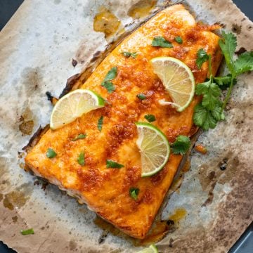 Baked salmon made with a lime and chili marinade shown atop a baking sheet with lime slice and chopped celery