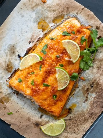 Baked salmon made with a lime and chili marinade shown atop a baking sheet with lime slice and chopped celery