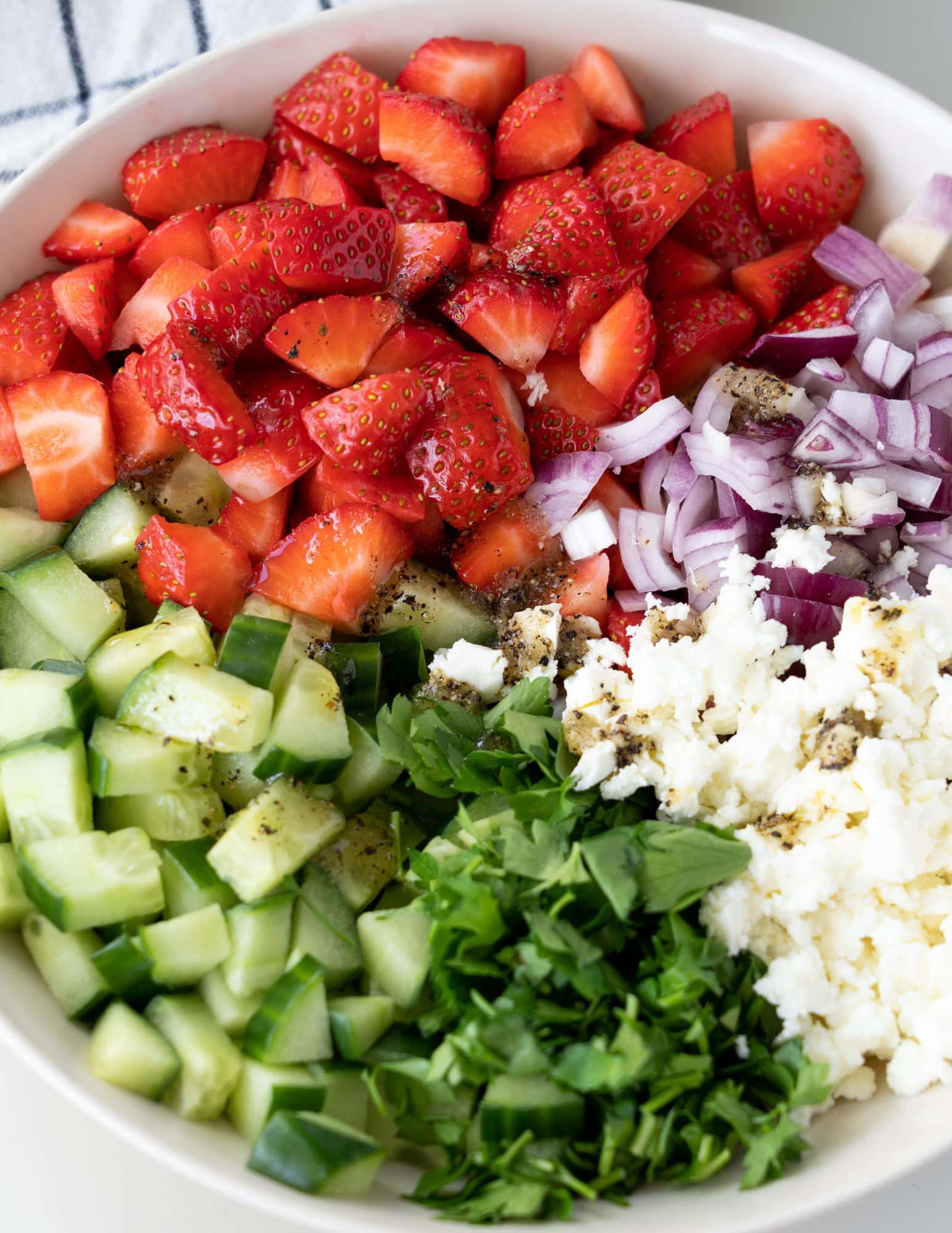 Close up image of ingredients of cucumber strawberry salad - strawberry, cucumber, onions, cheese and mint.