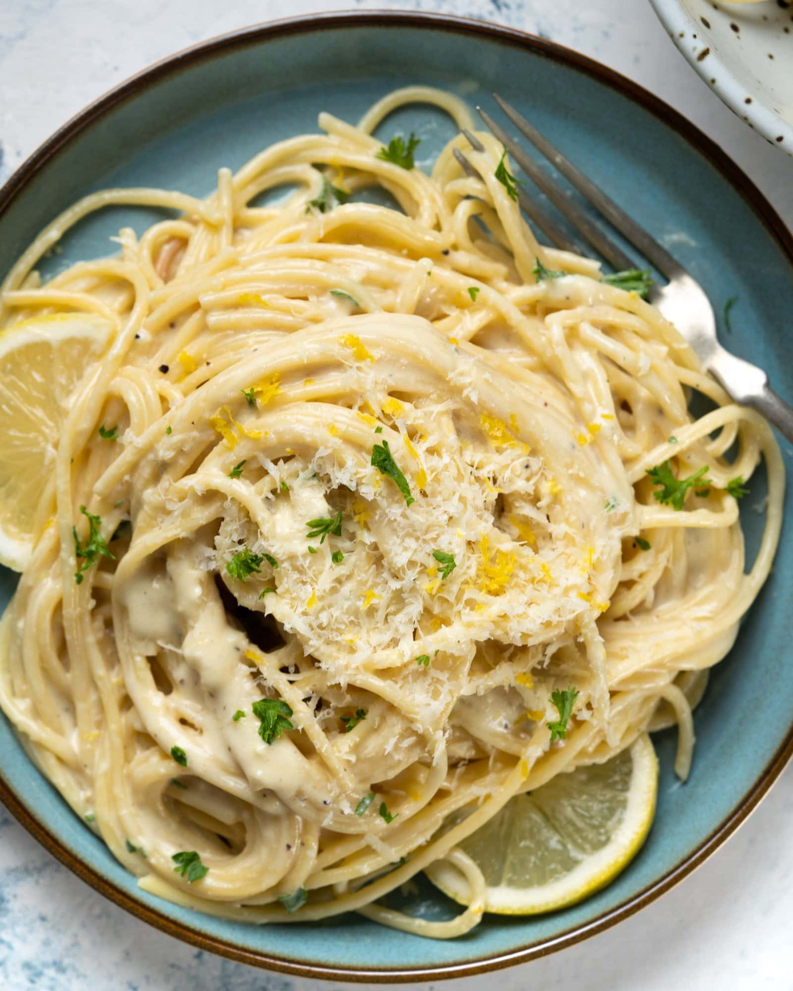 One-pot lemon pasta served on a blue plate and grated parmesan sprinkled on it.