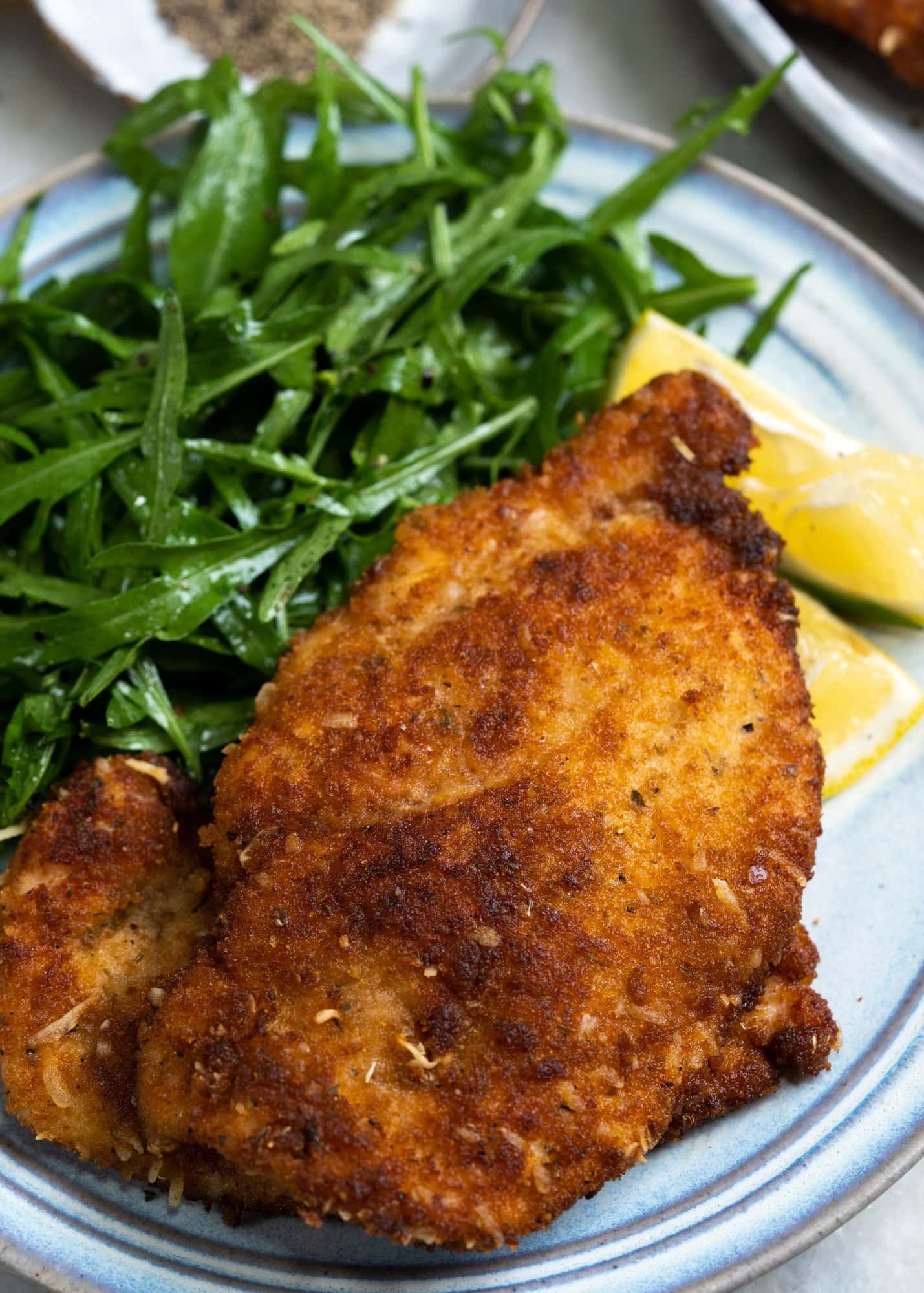 Chicken cutlets with a crisp coating made with Italian seasoning and served with lemon and arugula on a plate.