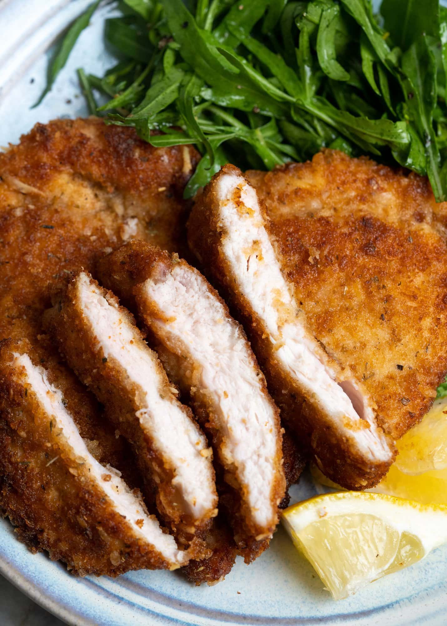 Chicken cutlet cut to show juicy chicken inside a crispy outer coating and served on a
