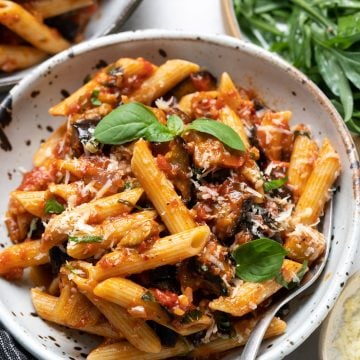 Pasta Alla Norma served with basil and shredded cheese as garnish.