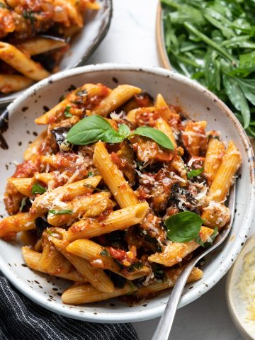 Pasta Alla Norma served with basil and shredded cheese as garnish.