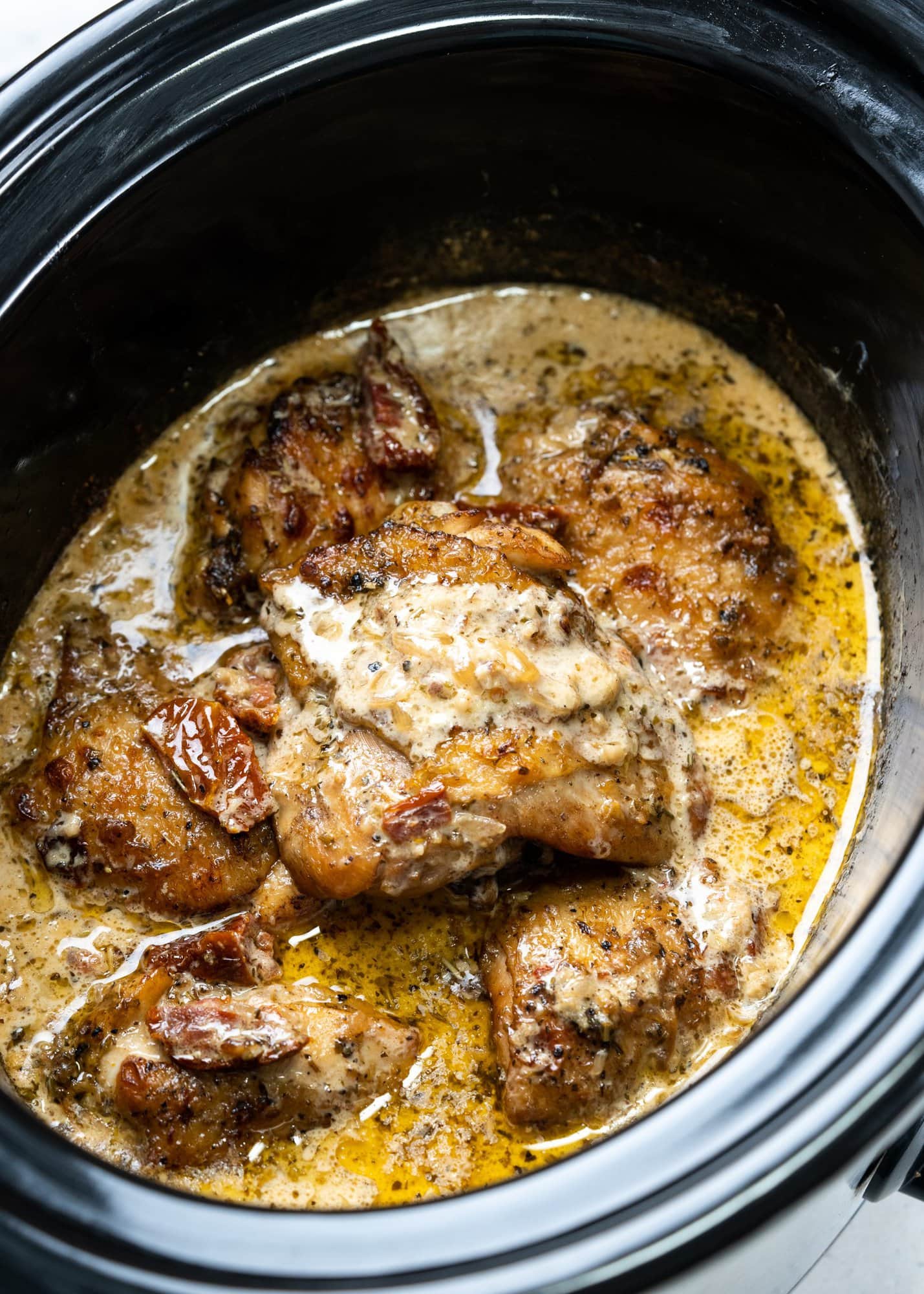 Close up of seared chicken thighs with crispy skin in a creamy sun-dried tomato sauce.