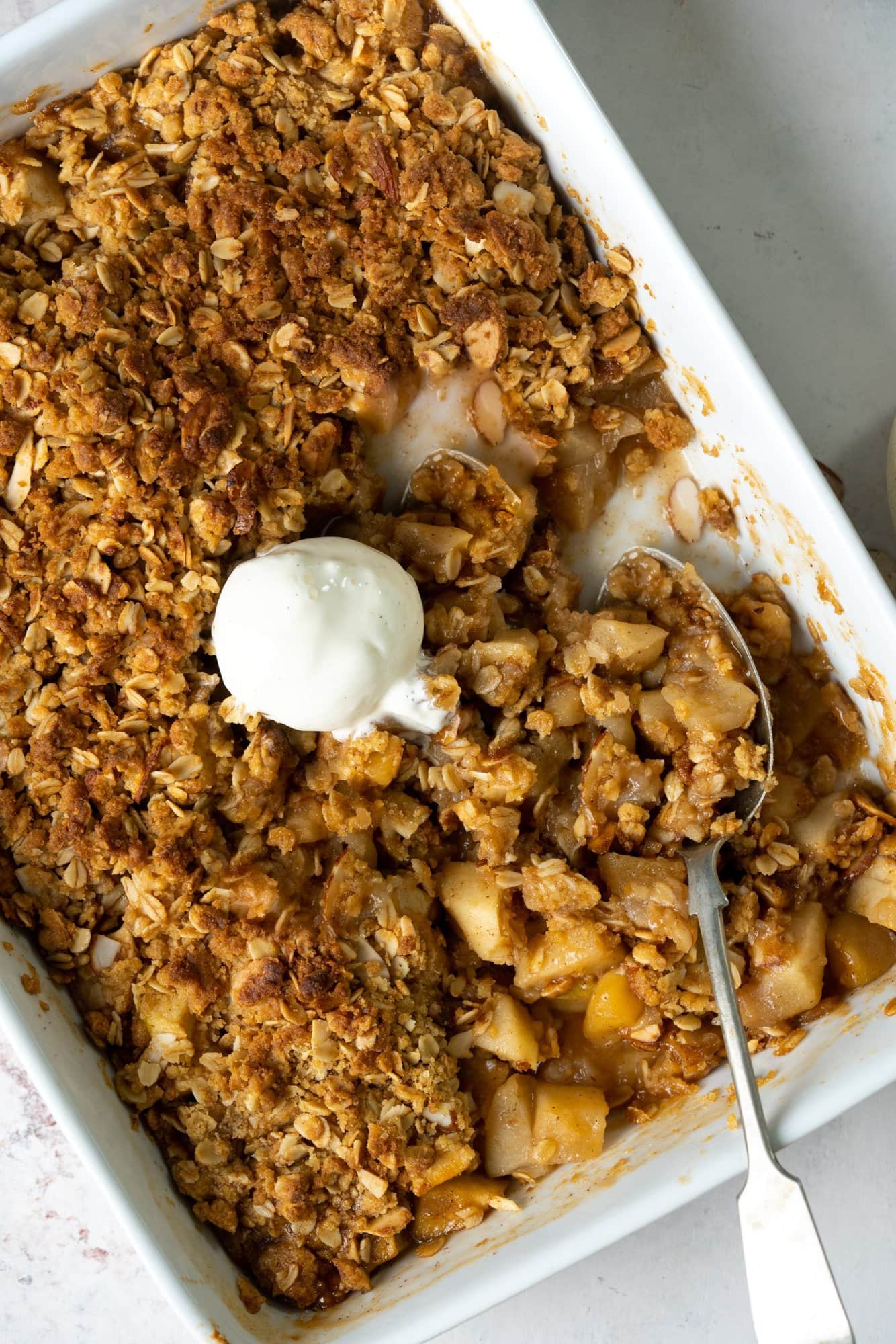 Apple crisp in a baking tray with a scoop of vanilla ice cream on top