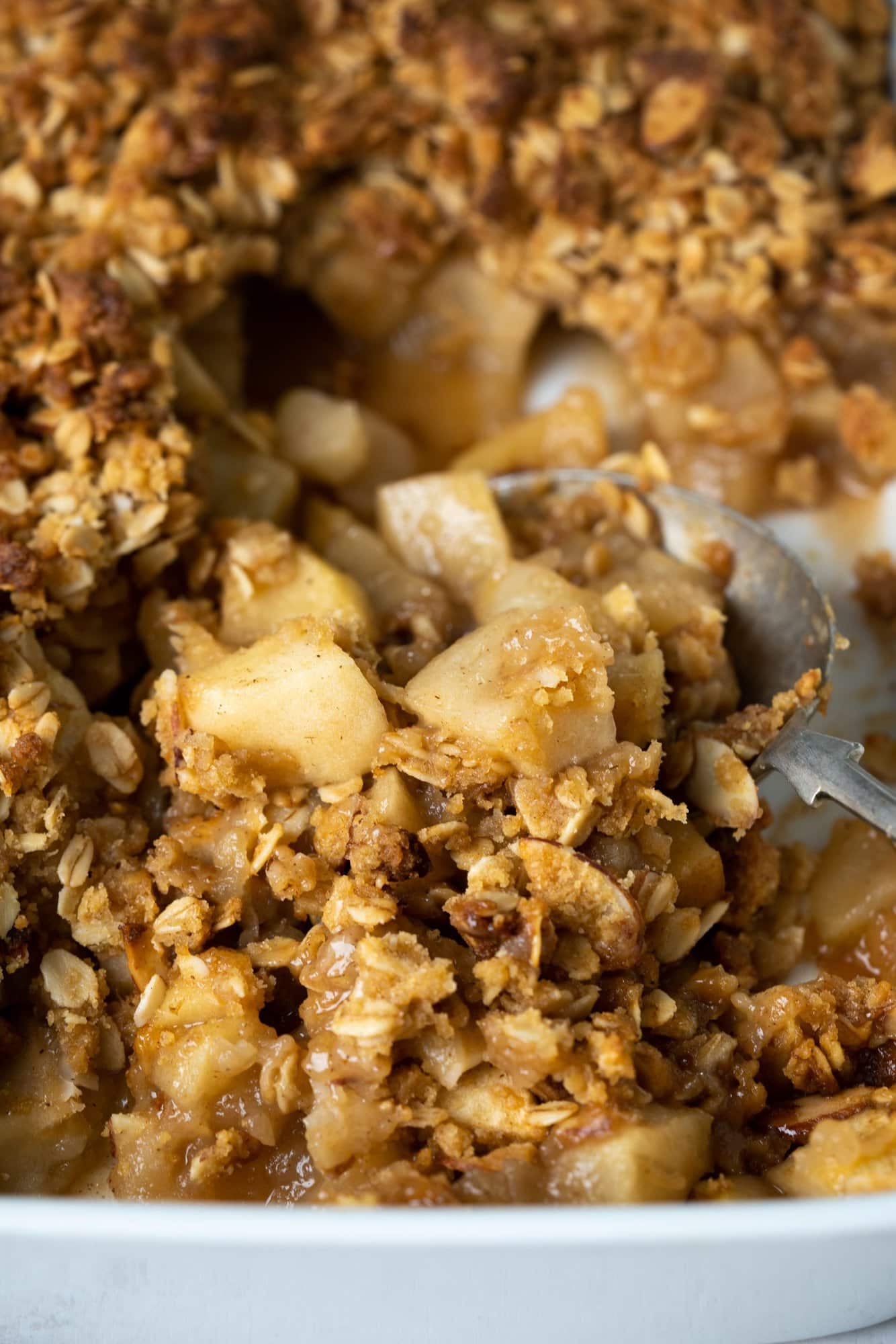 Close up image showing crispy oats, almond flakes and cooked apples in apple crisp