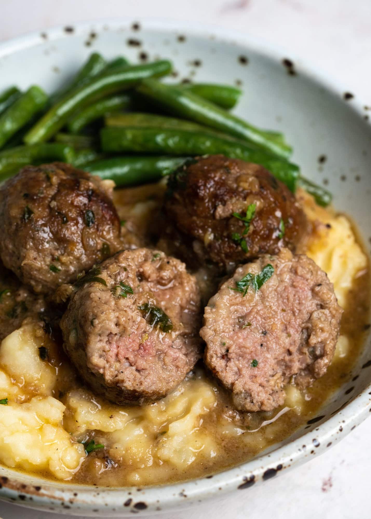 Meatballs sliced into half showing tender and juicy core on a bed of mashed potato.