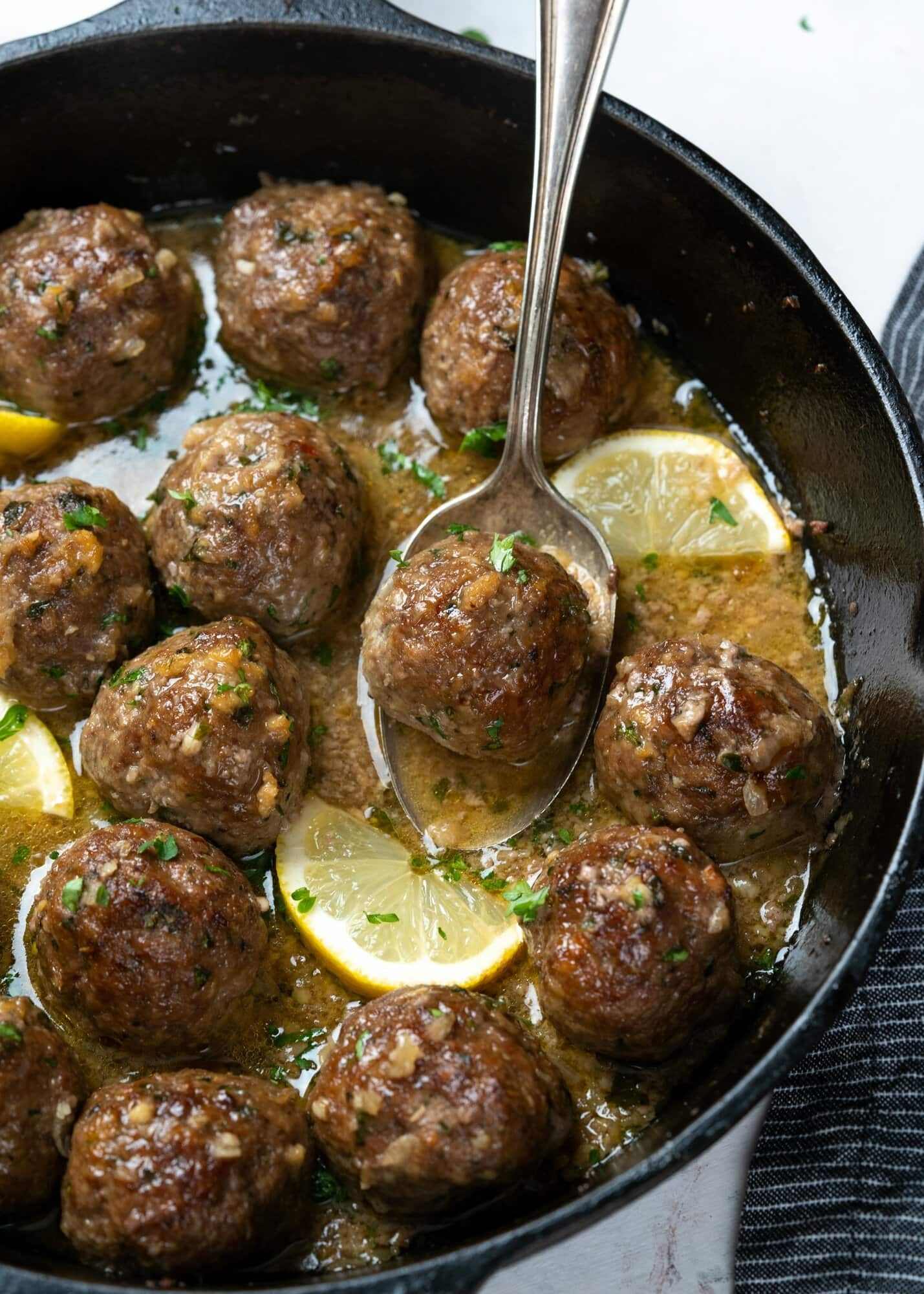meatball on a spoon with butter garlic sauce and lemon slices