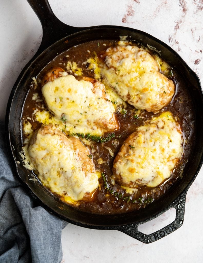 Chicken breast topped with cheese in a skillet of french onion gravy