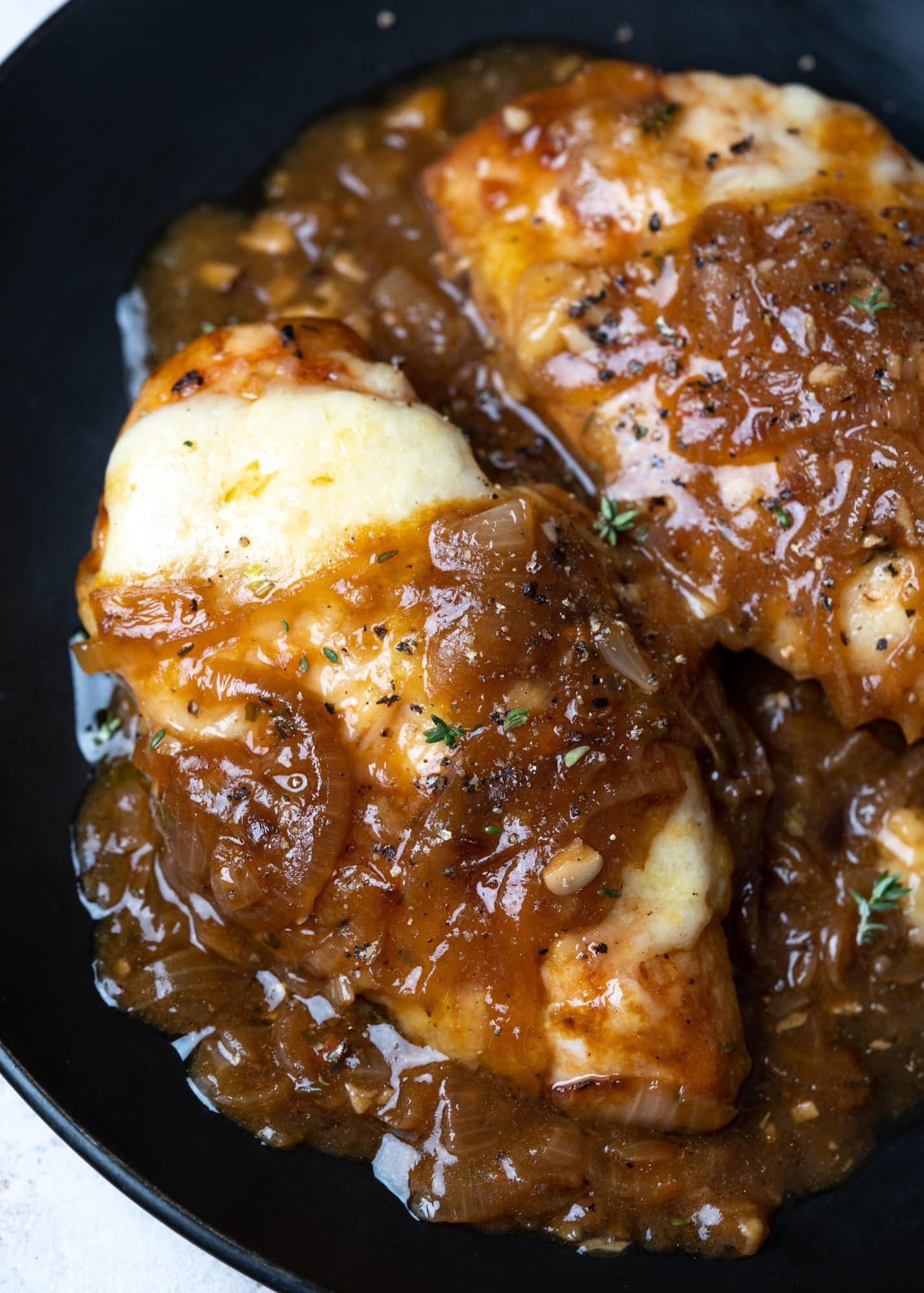 Close up of chicken topped with gruyere cheese in a caramelized onion gravy.