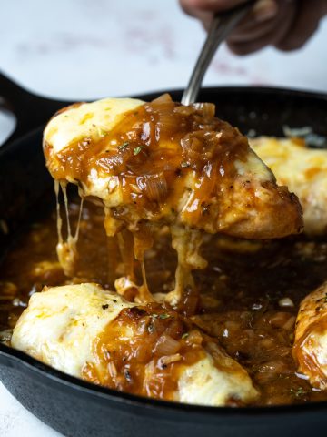 Picking a chicken breast topped with gruyere cheese from a saucy french onion gravy