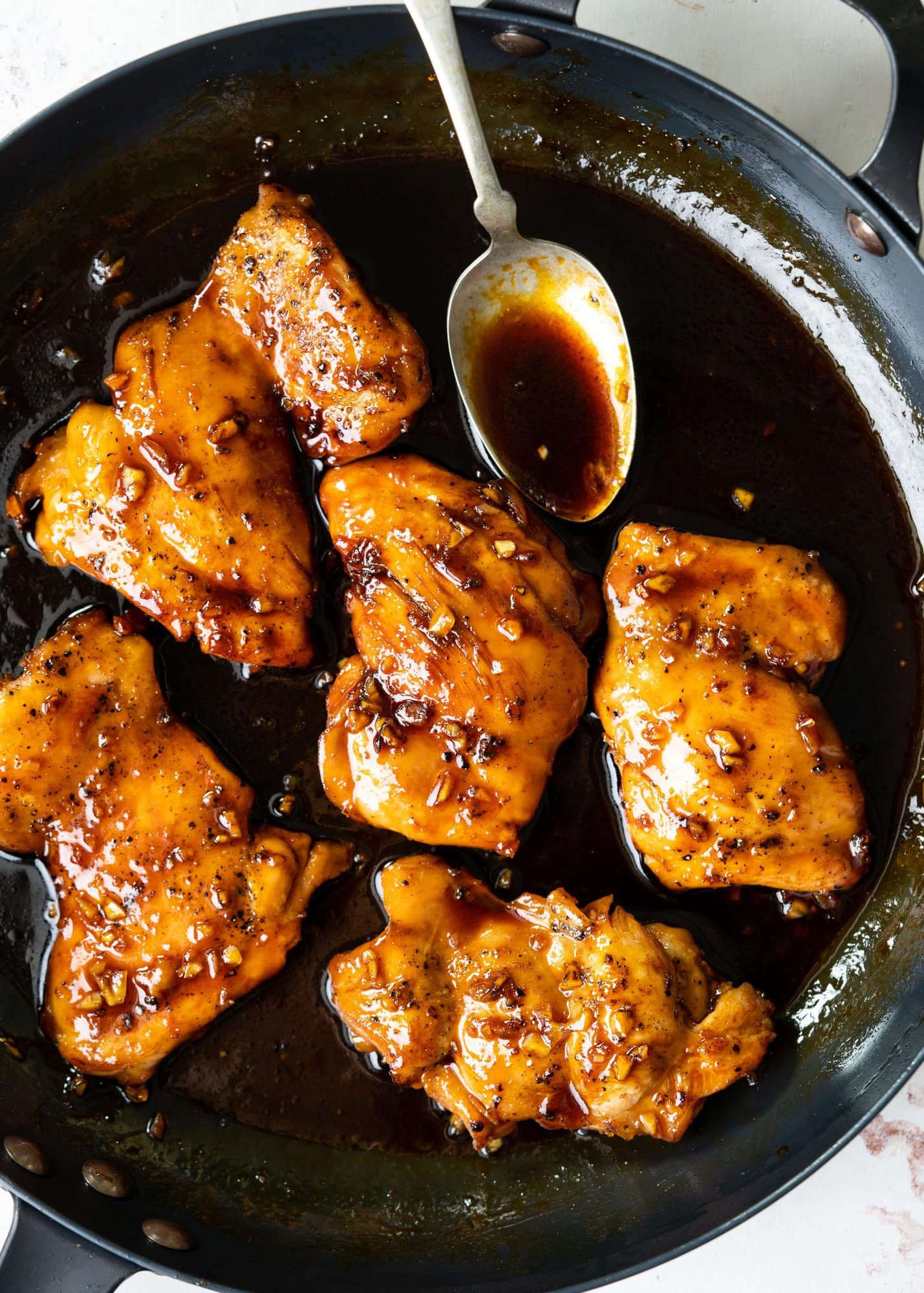 Spoonful of honey garlic sticky glaze sauce from a pan with chicken thighs.