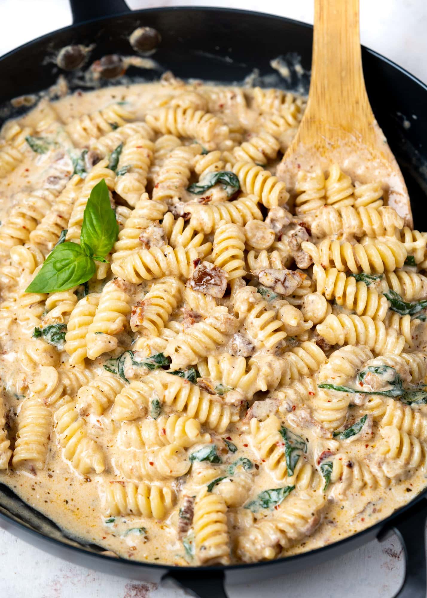 Close up of sun-dried tomato pasta made in a skillet with basil and ladle.