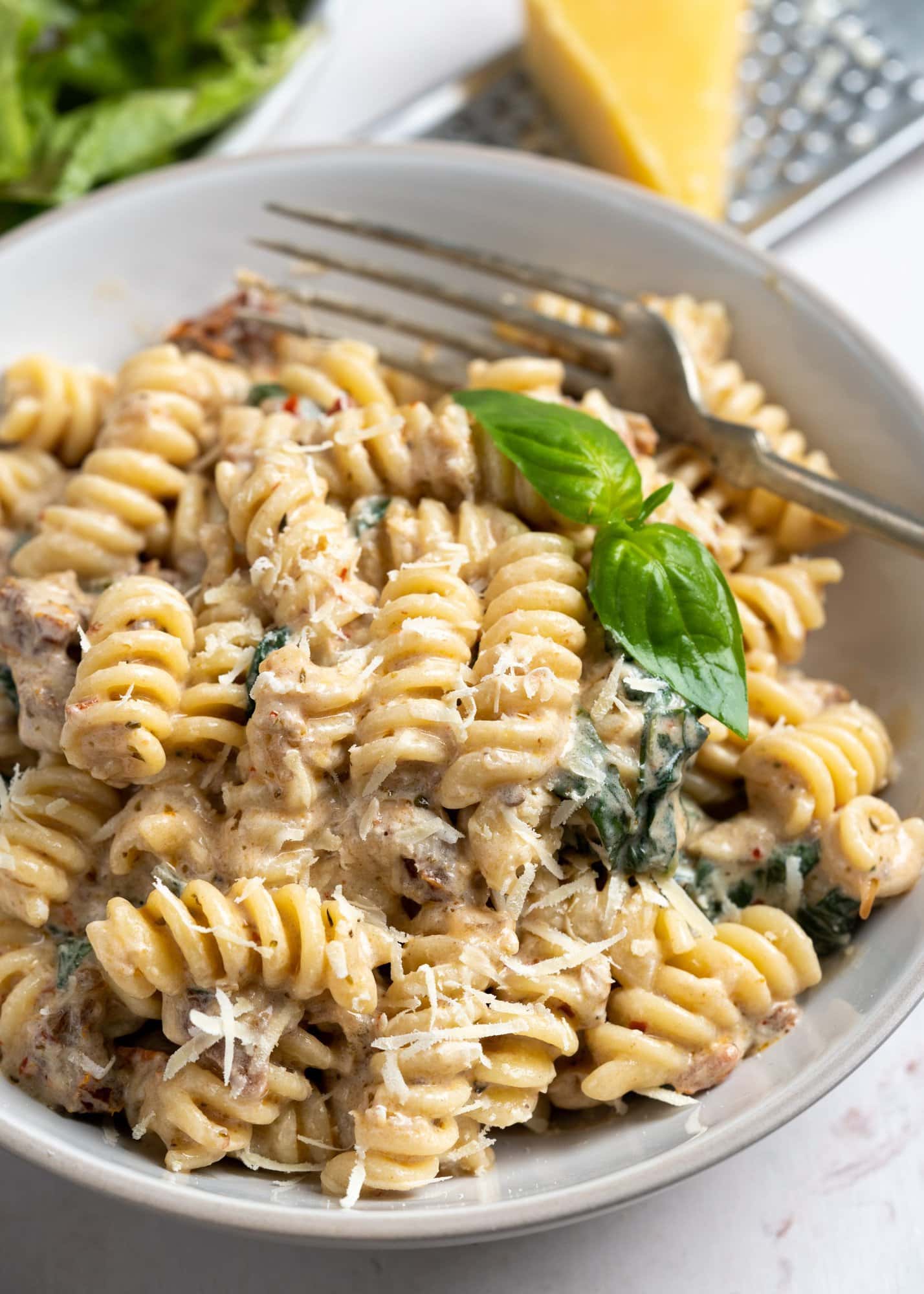 Sun-dried tomato pasta served in a white bowl with parmesan and basil as garnish.