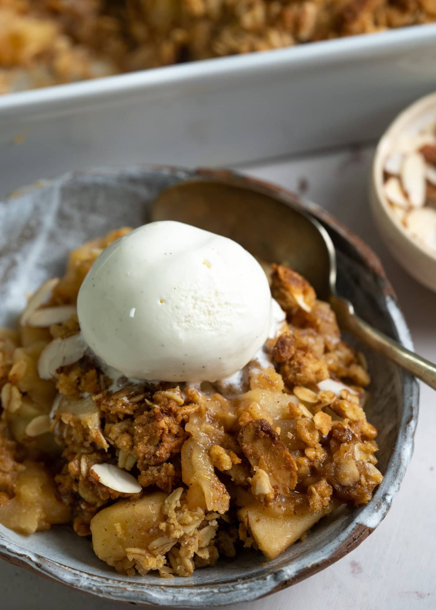 Apple crisp served on a bowl with a scoop of vanilla ice cream on top and spoon.