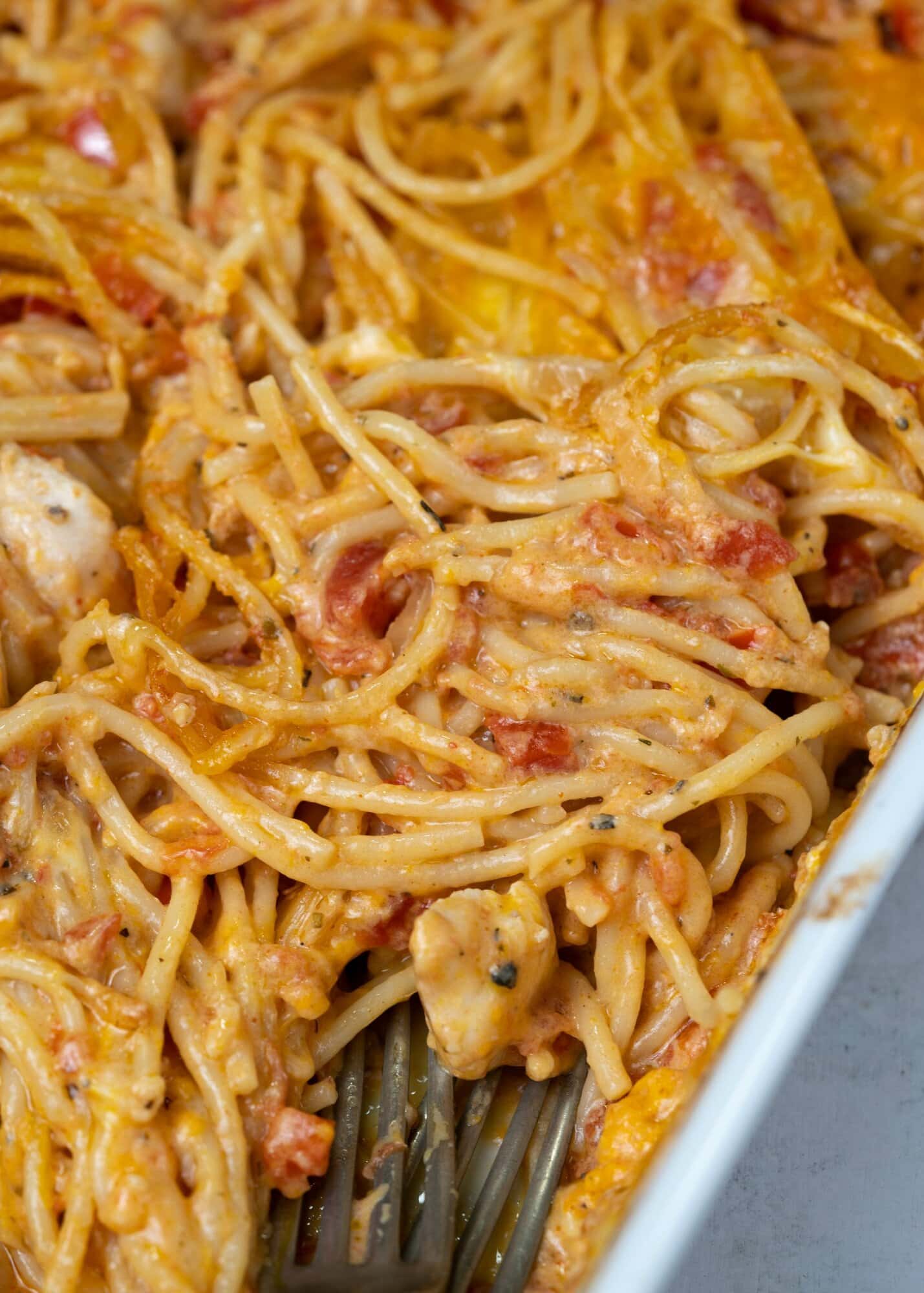 close up view of baked chicken spaghetti showing cheesy saucy spaghetti with chicken chunks 