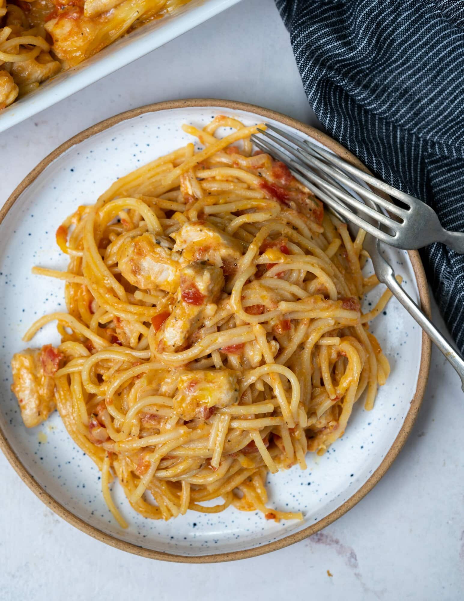 chicken baked spaghetti served in a white plate with a fork and spoon