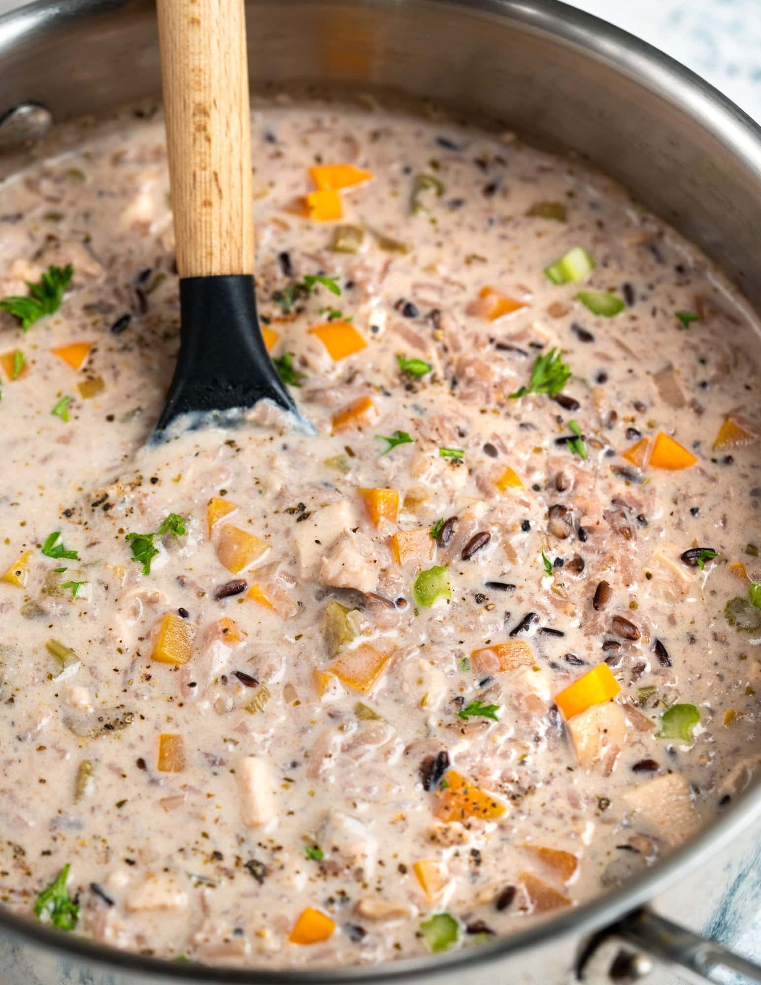 Pot of soup with flavorful wild rice cooked with chicken, mushrooms, chicken stock and vegetables shown with a ladle.