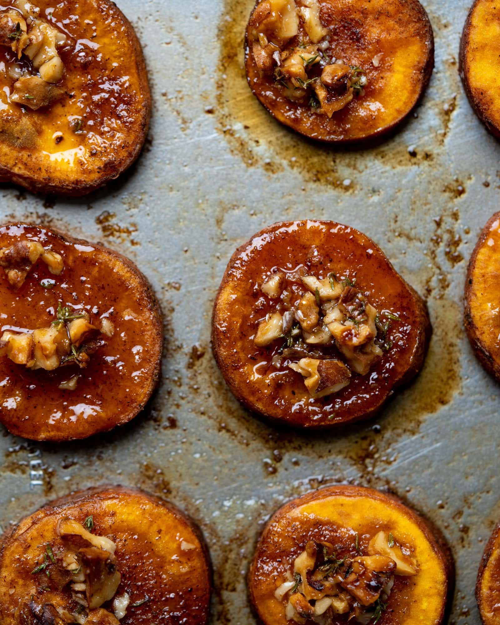 Sweet potatoes roasted to perfection on a baking tray. They have glaze from the maple syrup and have crunchy walnuts on top.