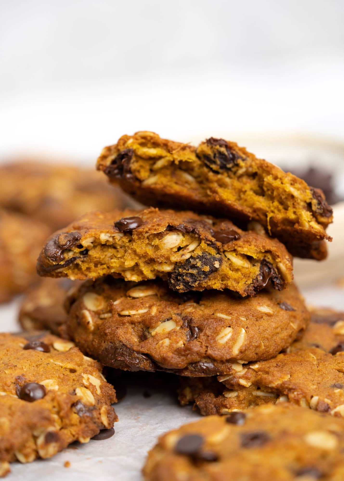 Close up image shows a stack of Pumpkin Oatmeal cookies with Chocolate Chip. Top two are cookies broken into halves showing soft and dense in the middle.