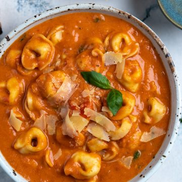 Tomato and tortellini pasta soup served in a white bowl.