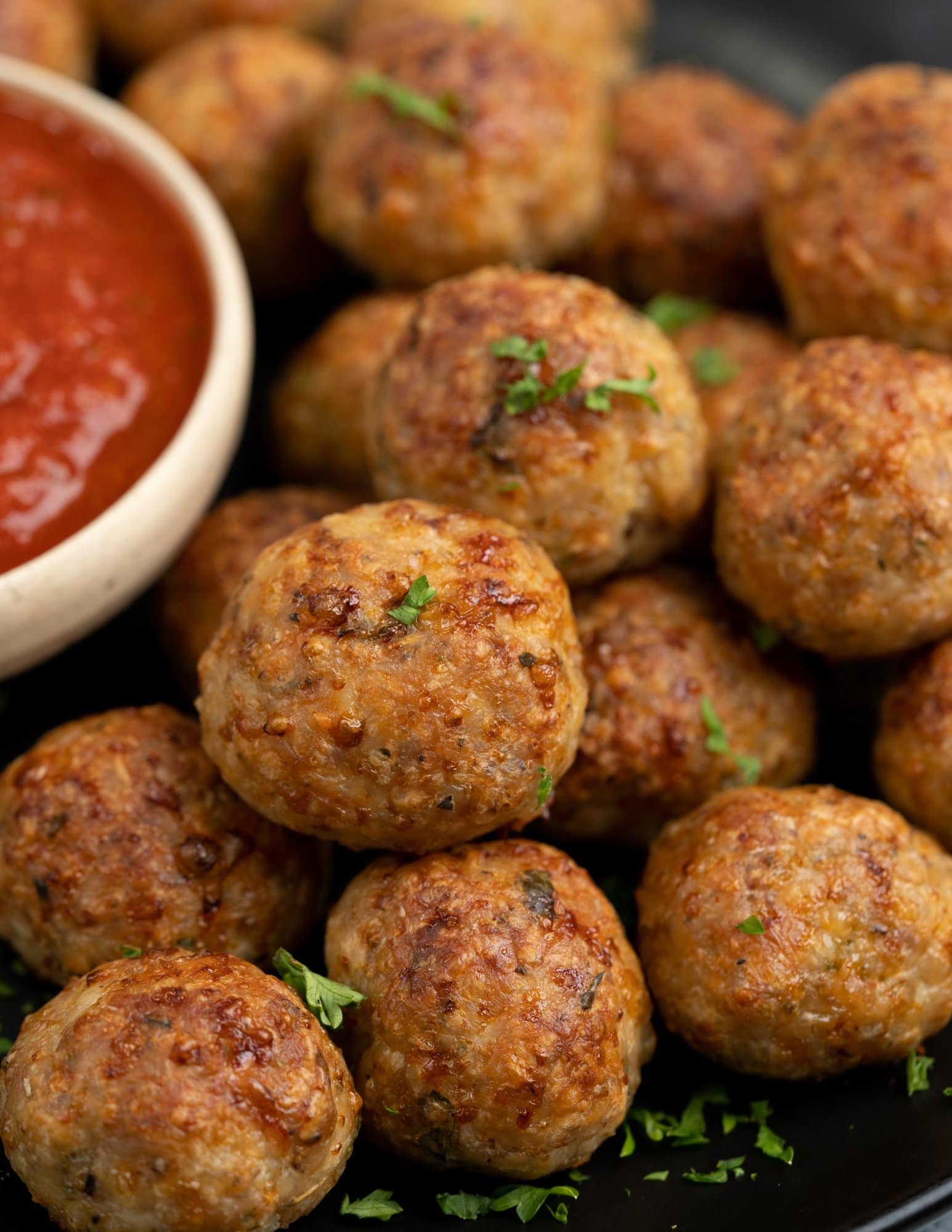 Close up view of golden brown chicken meatballs that are served with marinara sauce and sprinkled with chopped parsley.