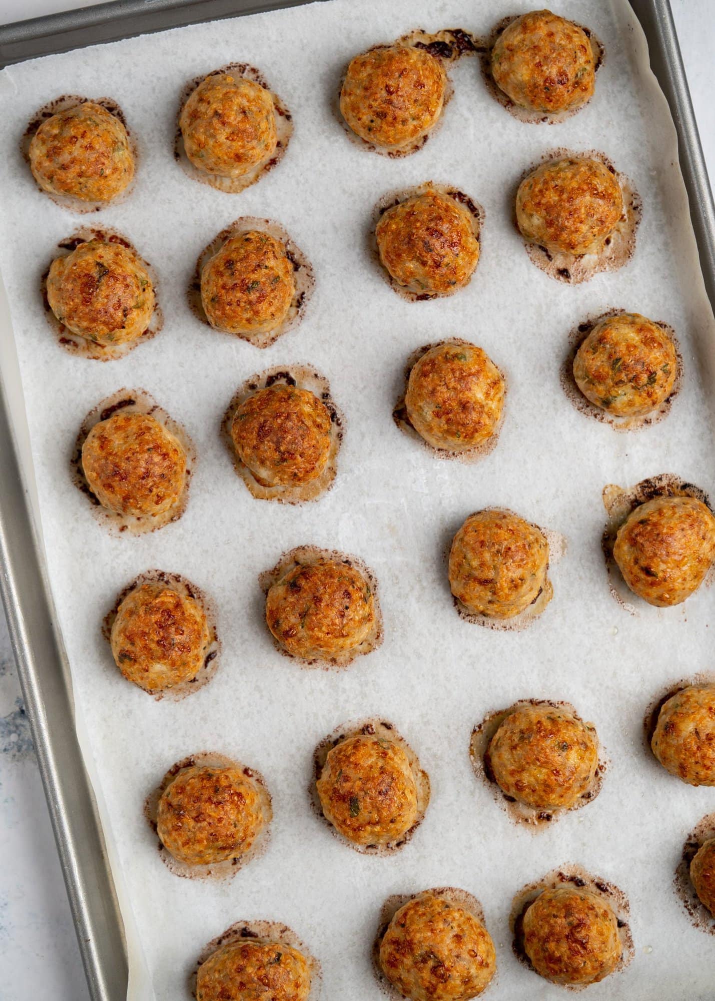 Chicken meatballs, on a baking sheet atop a tray, freshly baked. These meatballs have a golden brown color on the exterior.