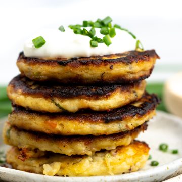 Stack of mashed potato pancakes made with crisp outside and soft cheesy inside. Served with sour cream and chopped green onion on top.