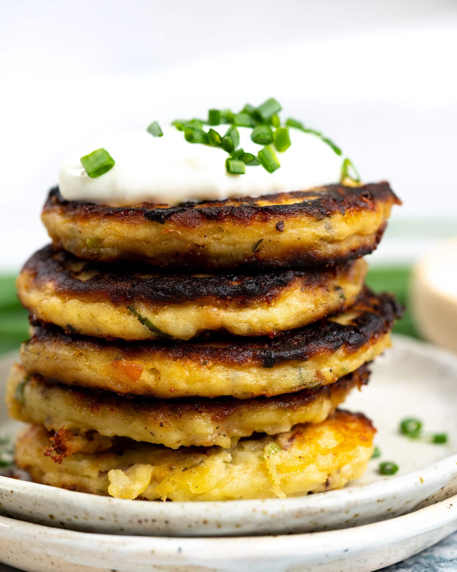 Stack of mashed potato pancakes served with a dollop of sour cream and sprinkled green onions on top.