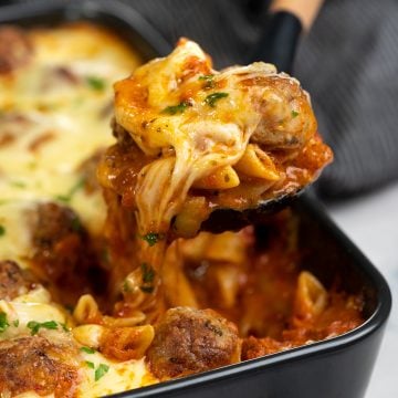 Slice of meatball casserole picked with a spatula showing strands of cheese and saucy pasta along with chunks of tender meatball