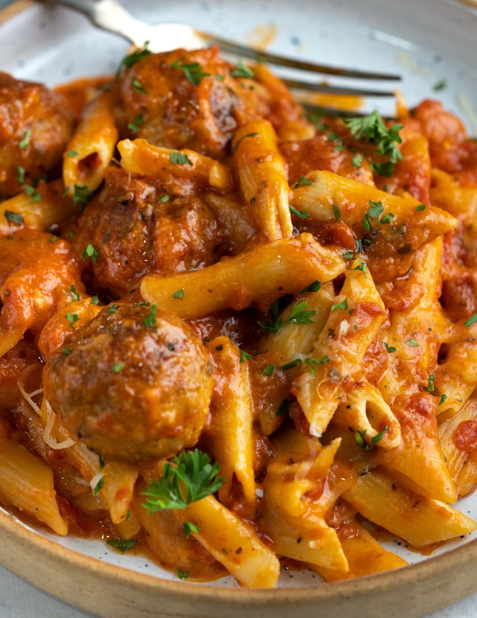 Tangy meatball casserole served in a bowl garnished with some chopped fresh parsley. 