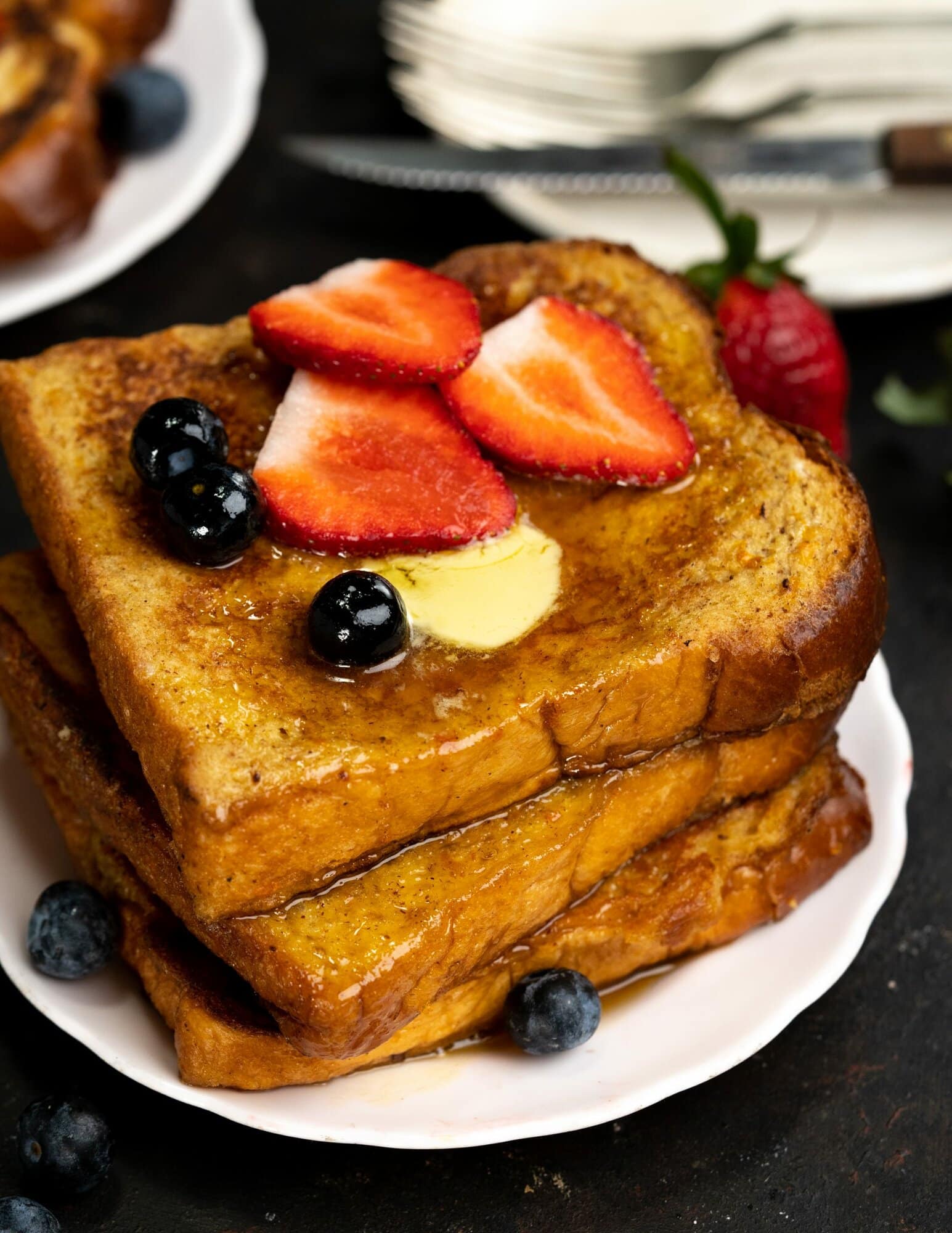 Top view of a stack of brioche toasts which is topped with maple syrup. butter, blueberries and slices of strawberry