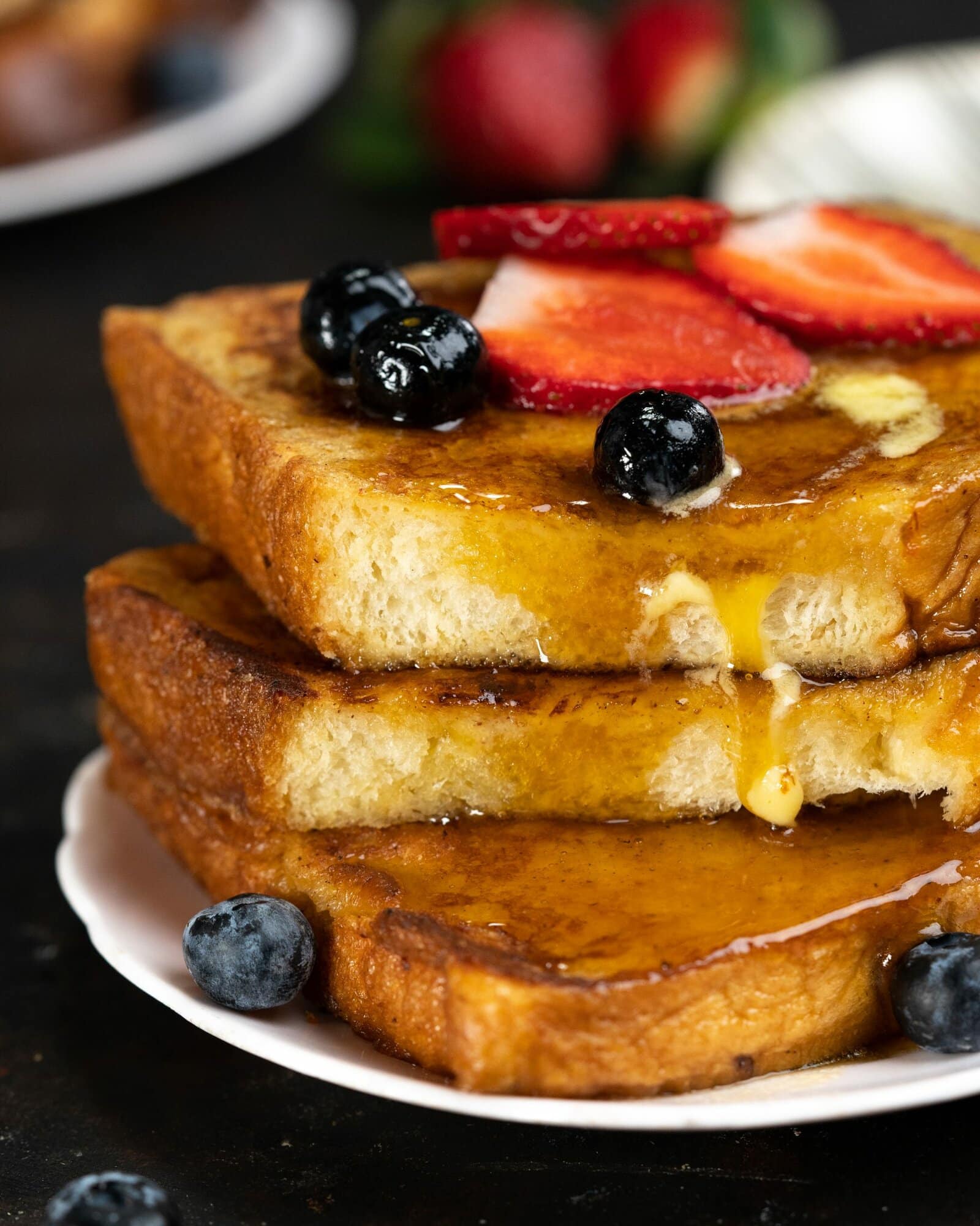 maple syrup dripping down the sides of a stack of brioche bread toasts. it is adorned with berries.