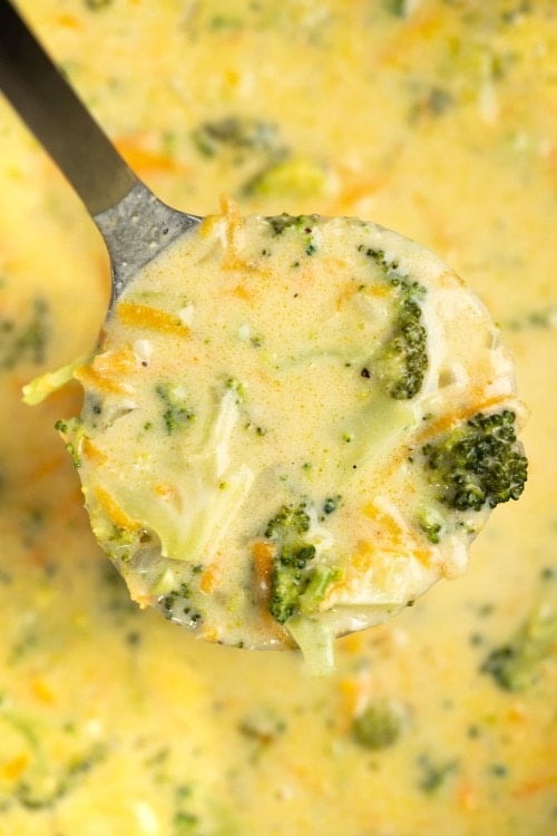 Ladle showing broccoli, sliced carrots in a cheesy soup made with cheddar.