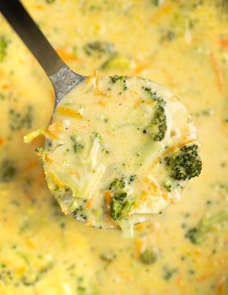 Ladle showing broccoli, sliced carrots in a cheesy soup made with cheddar.