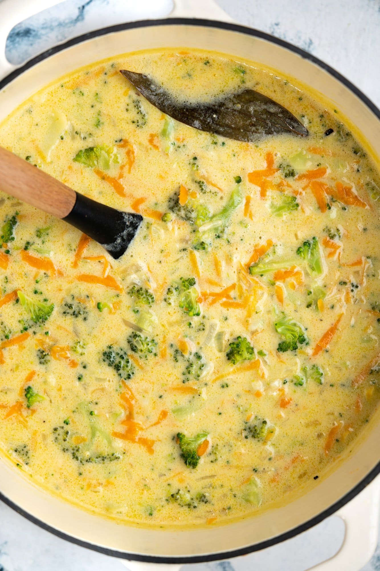 Broccoli cheddar cheese soup is cooked in a dutch oven with spices and herbs.