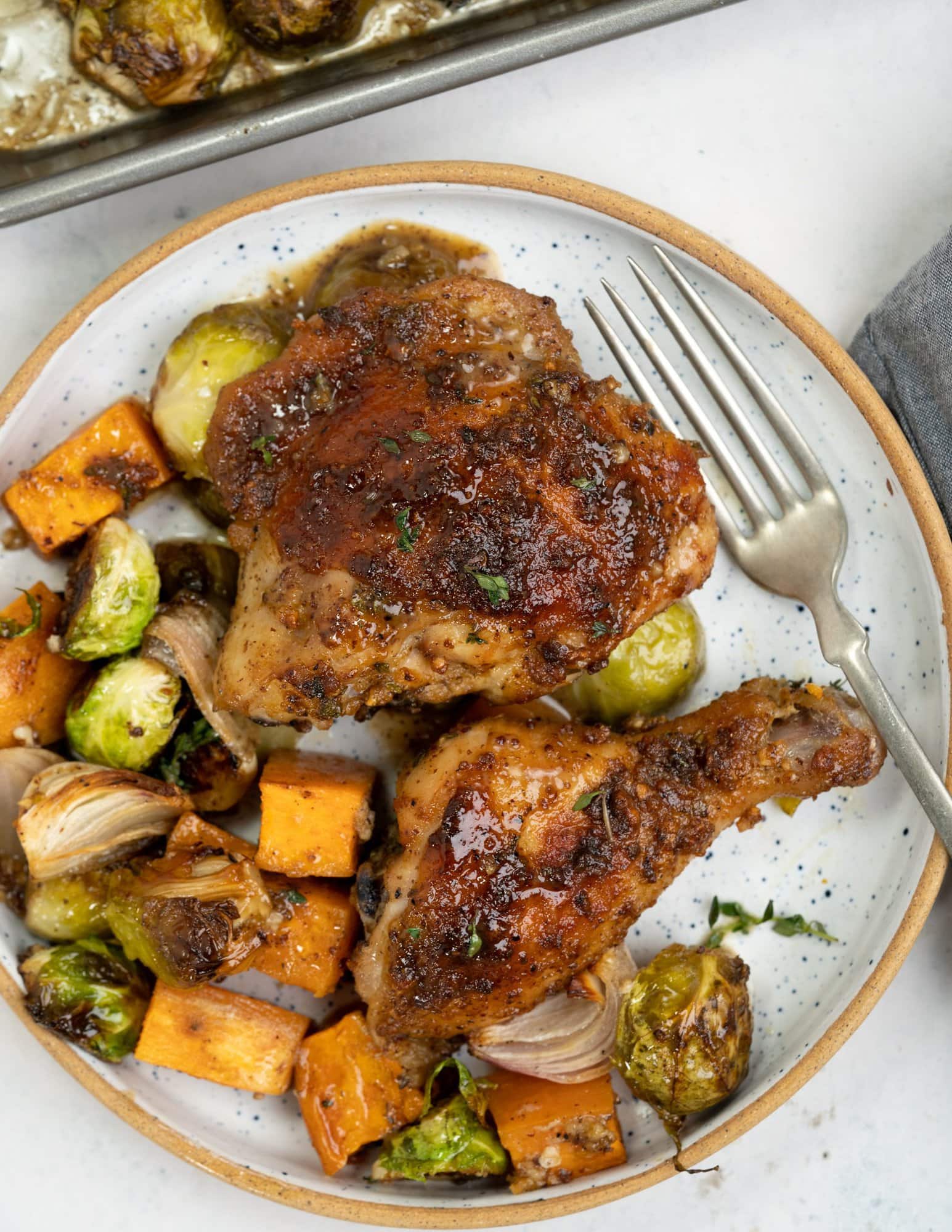 Sheet pan roasted chicken thigh and leg with a brown crust and maple mustard dressing glaze served on a plate along with veggies