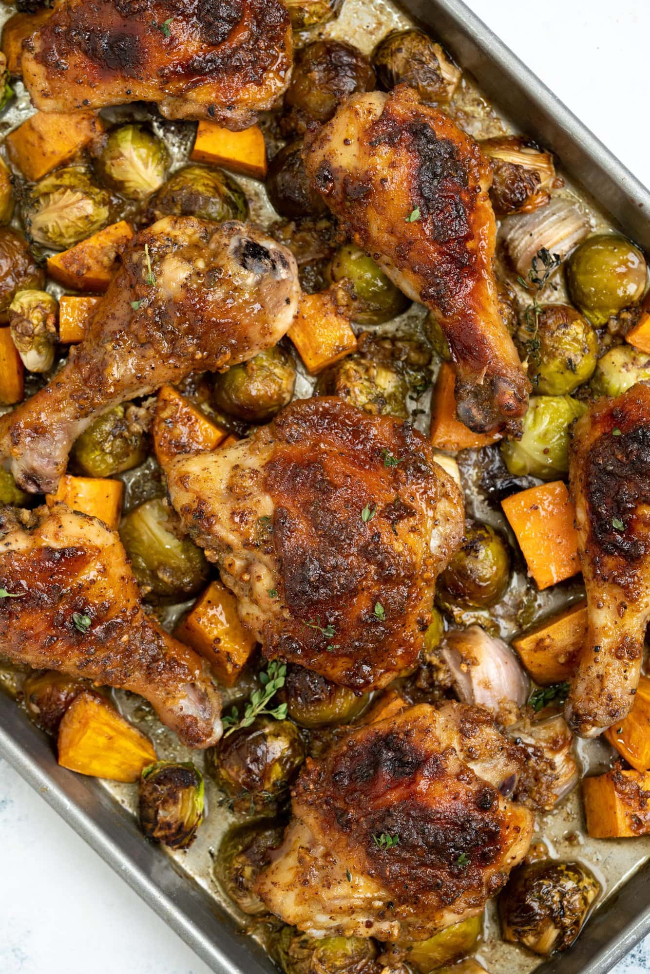 Chicken legs and thighs are baked along with brussel sprouts, sweet potatoes and onions, with a maple mustard dressing in a sheet pan.
