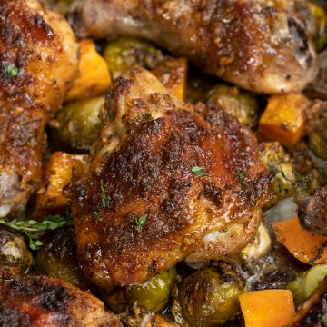 Close up view of brown crust and glaze on top of roasted chicken done on a sheet pan along with veggies.