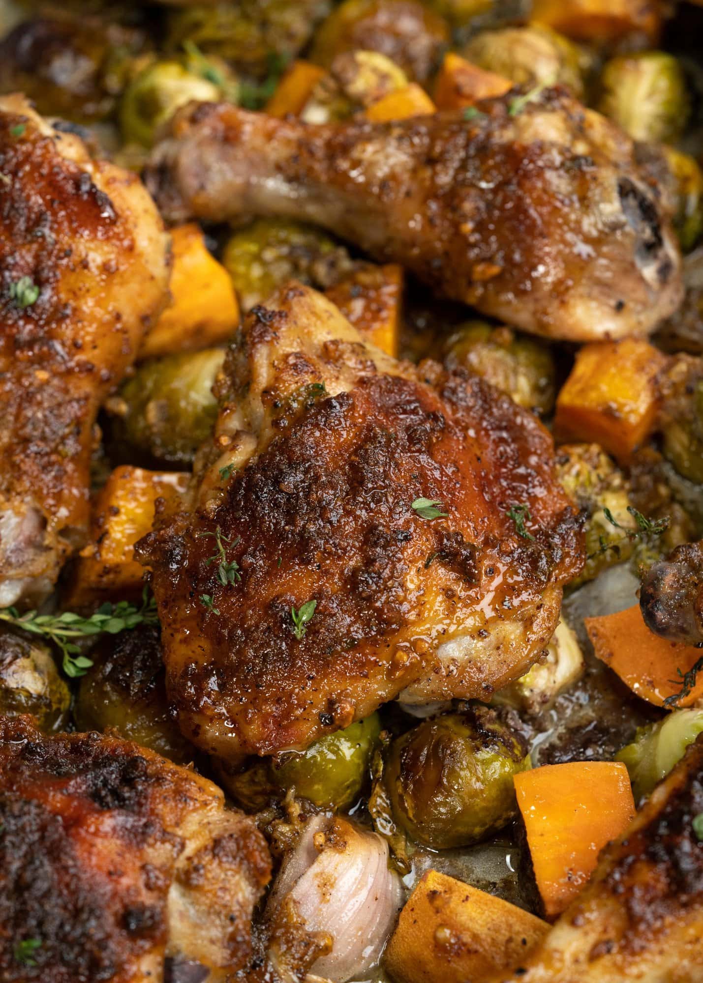 Close up view of brown crust and glaze on top of roasted chicken done on a sheet pan along with veggies.