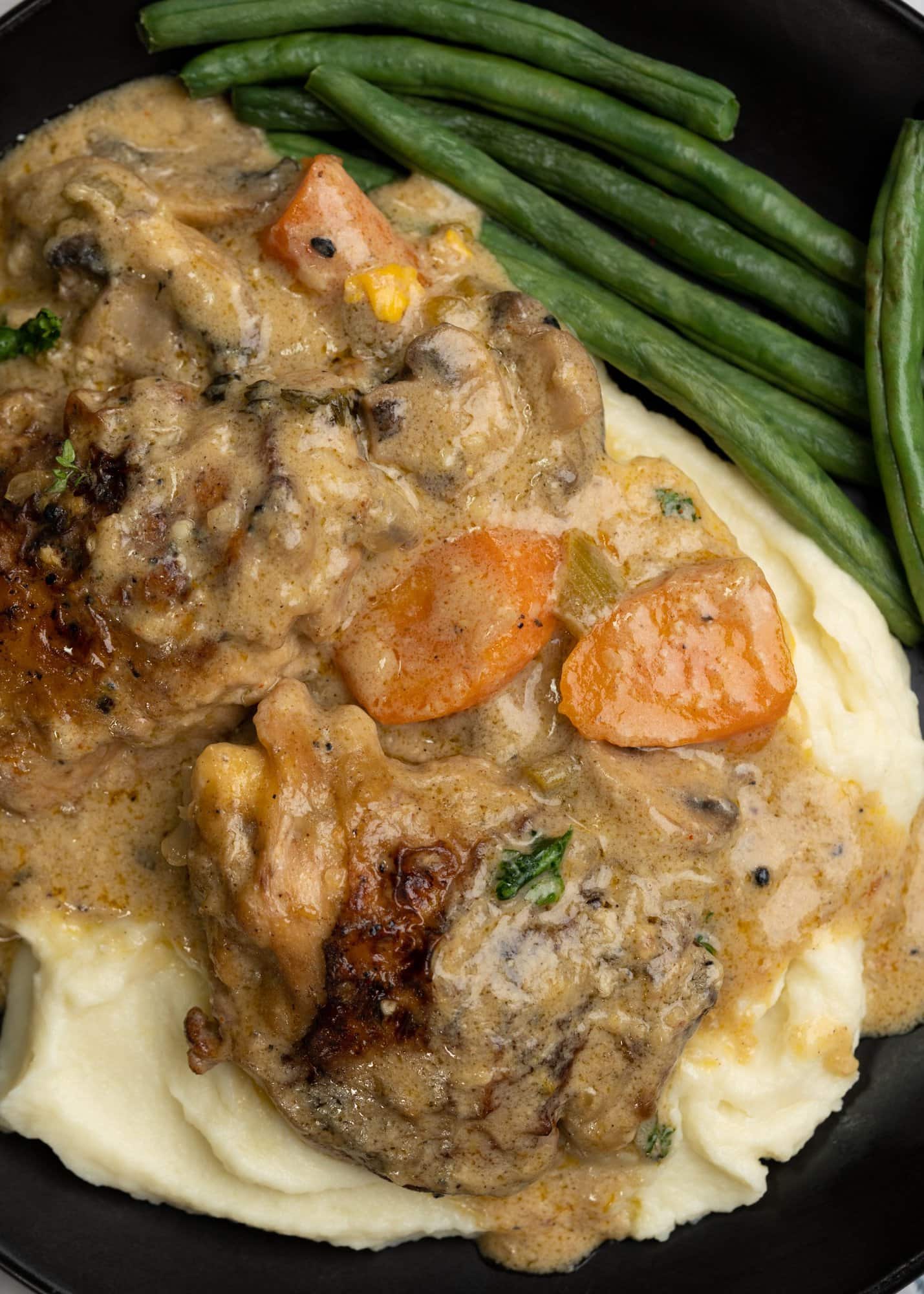 Seared chicken pieces and sauce from fricassee with carrots served on a bed of mashed potato and served with sauteed green beens. 