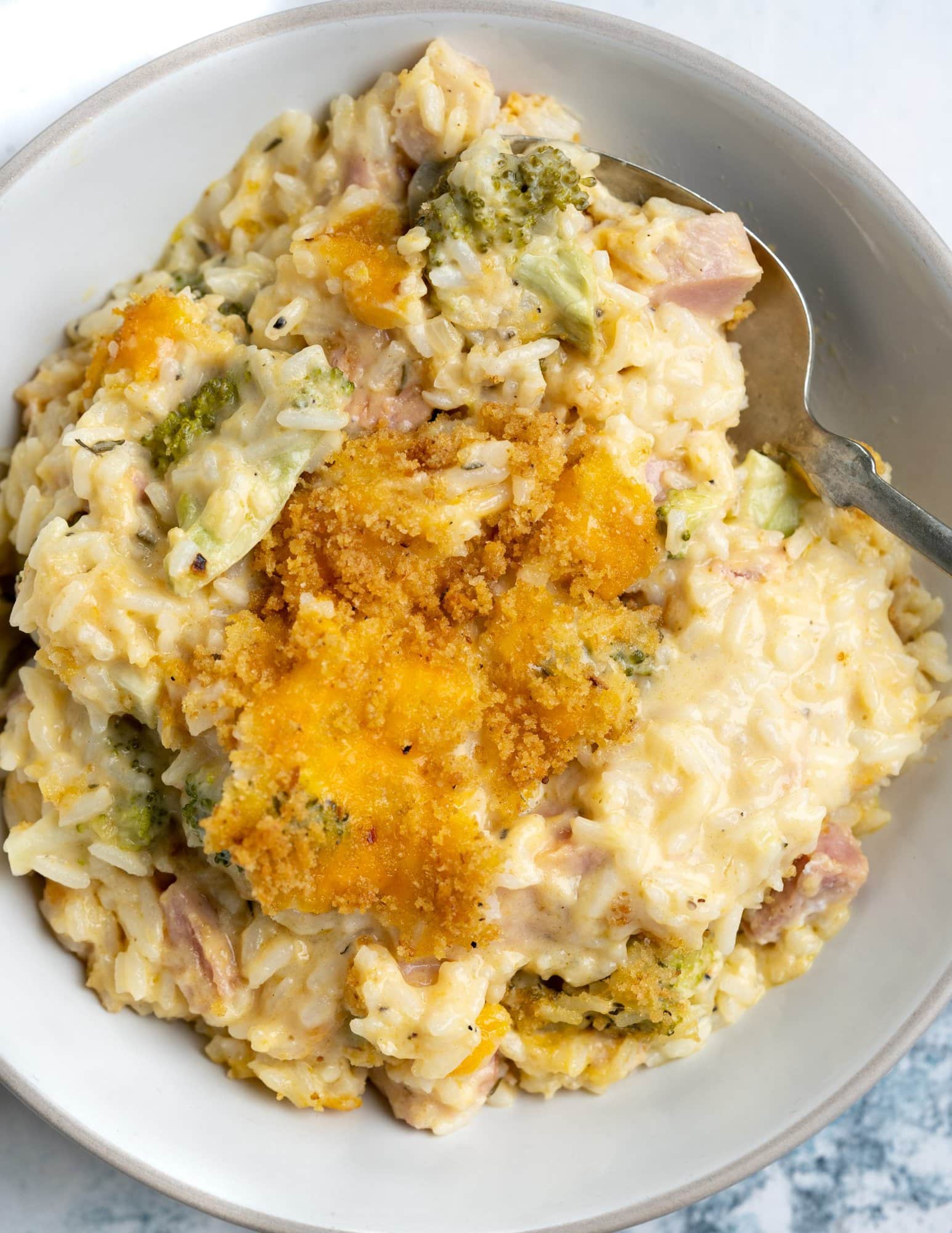 Ham casserole made with leftover ham, rice, broccoli and creamy sauce and a golden brown crusty top served in a white bowl and spoon.