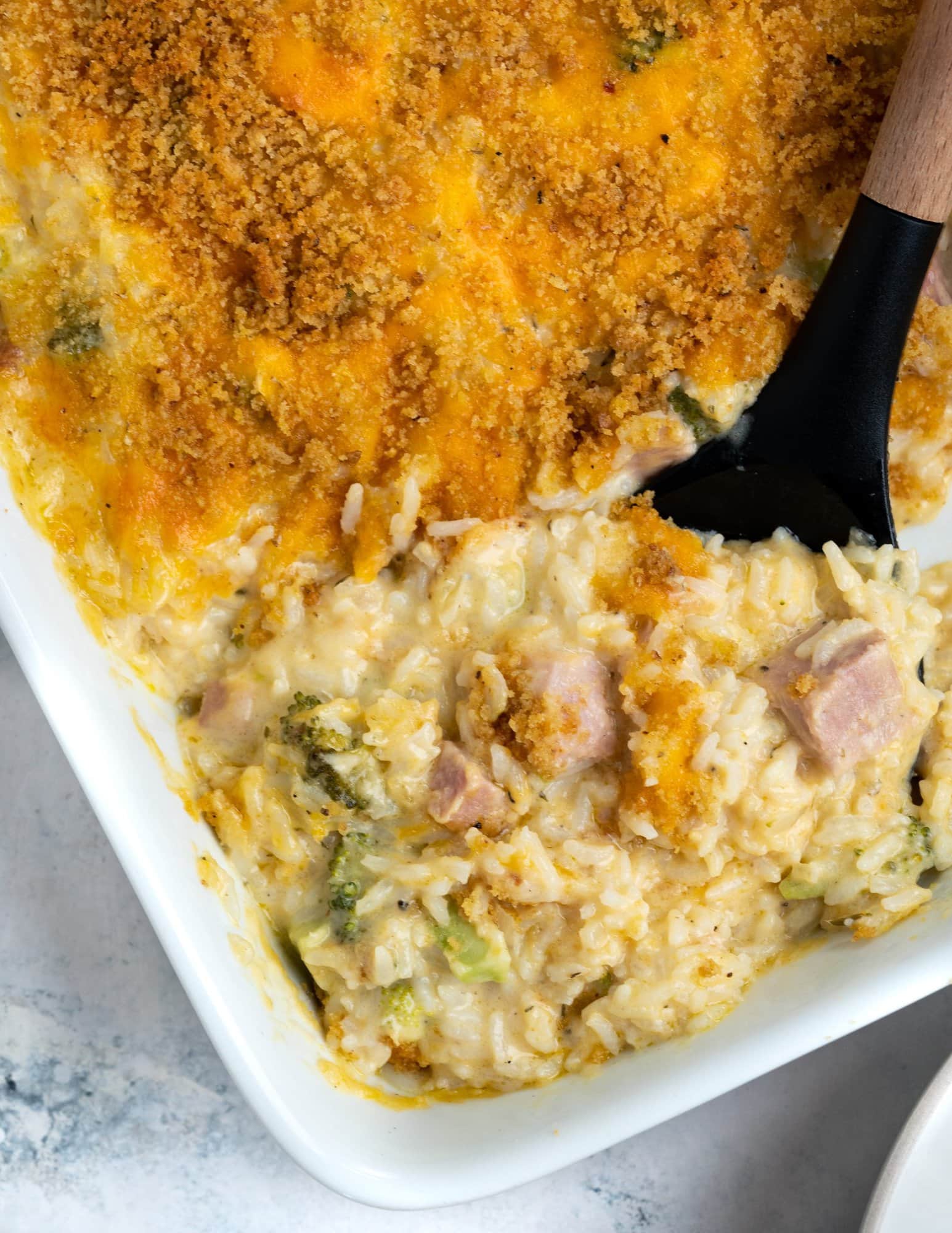 Corner of the casserole showing golden brown crust and underneath that a creamy mix of rice, ham, and broccoli.