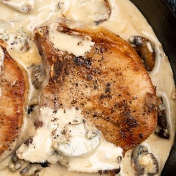Pork chop with a golden brown crust in a sea of creamy mushroom sauce