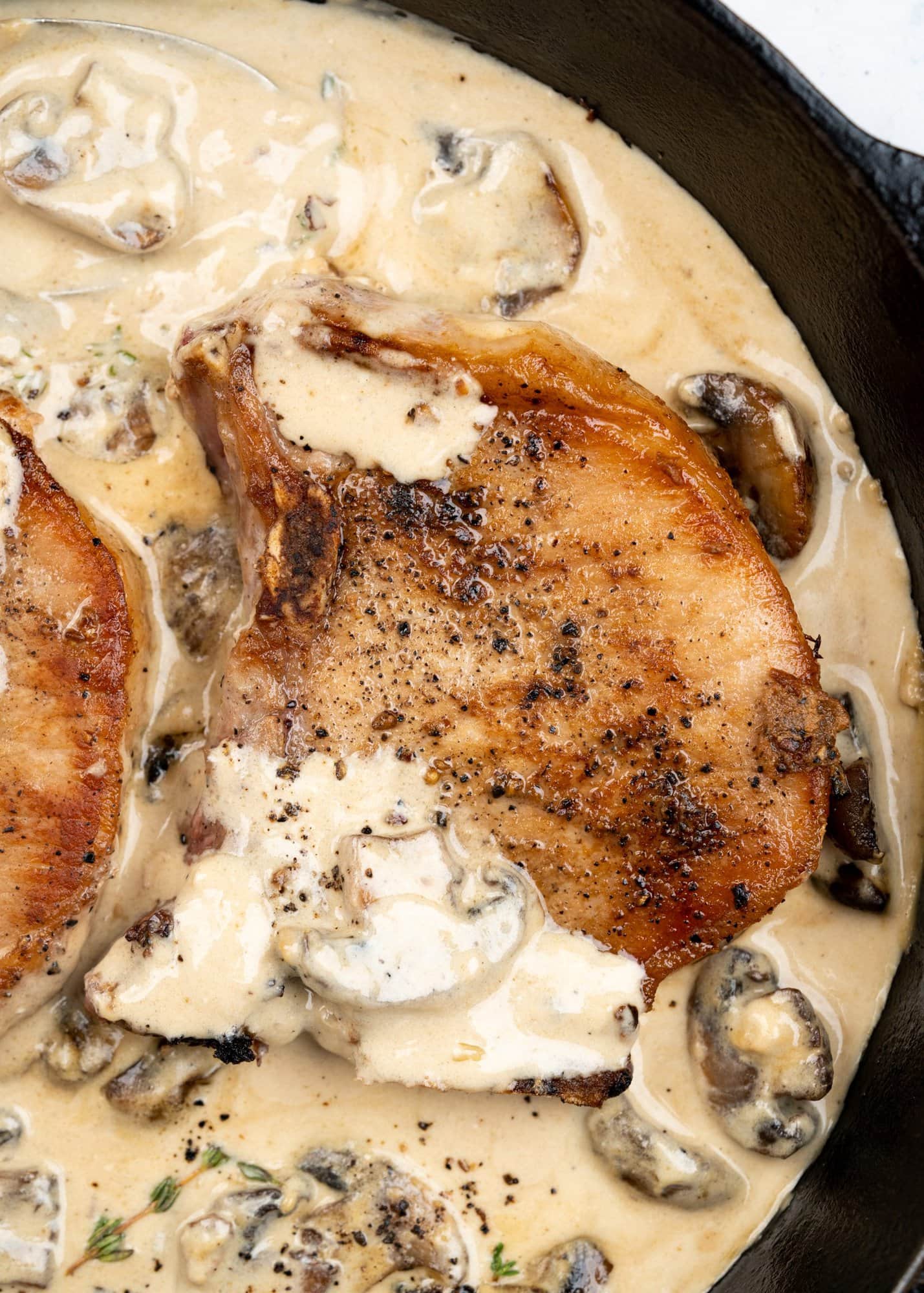 Close up image of seared pork chop with a golden brown crust in a sea of creamy mushroom sauce, made in a black skillet.