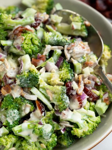 Close up view of broccoli salad shows tender yet crips, broccoli, chopped onions, bacon bits with a creamy yogurt dressing.
