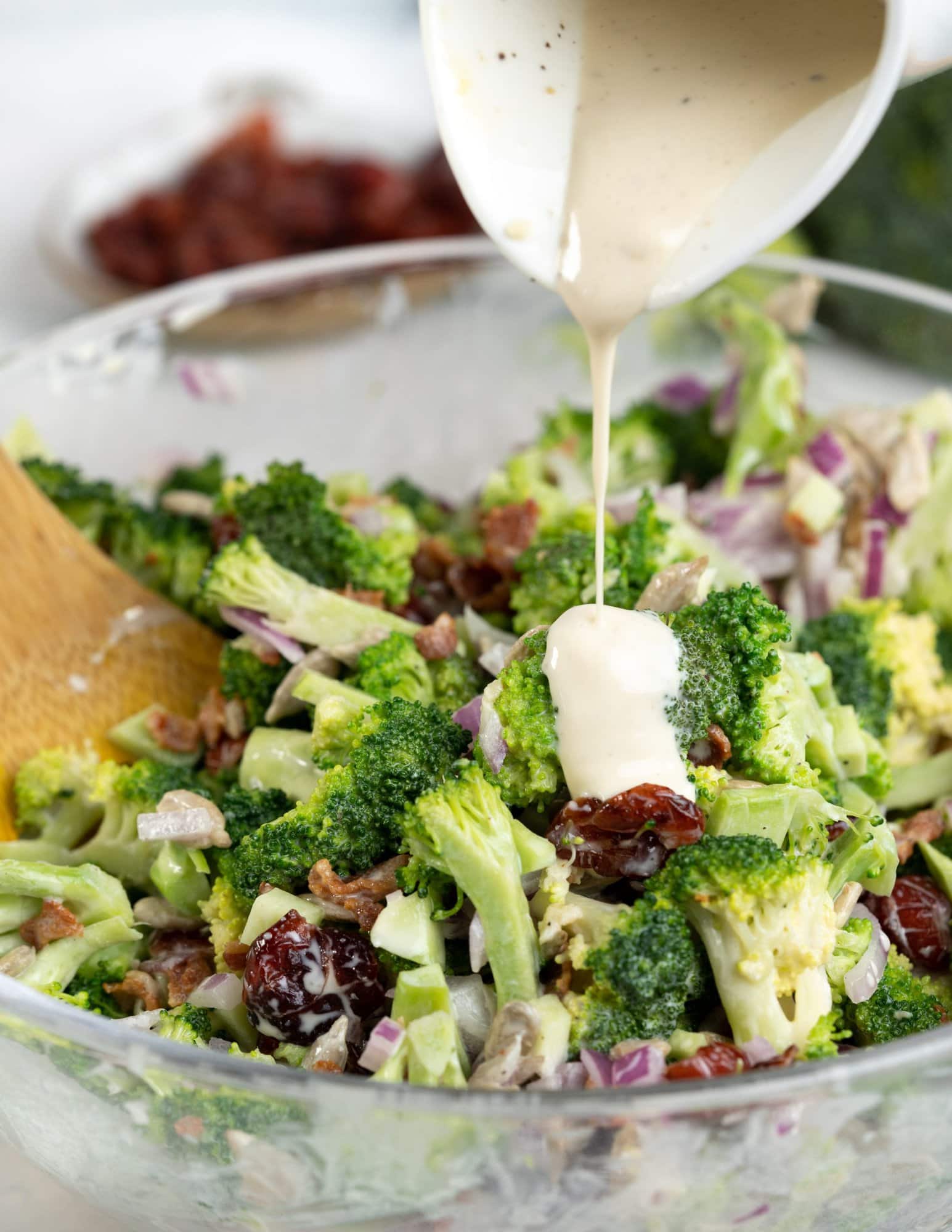 Creamy and light yogurt dressing drizzled over broccoli salad ingredients in a mixing bowl.