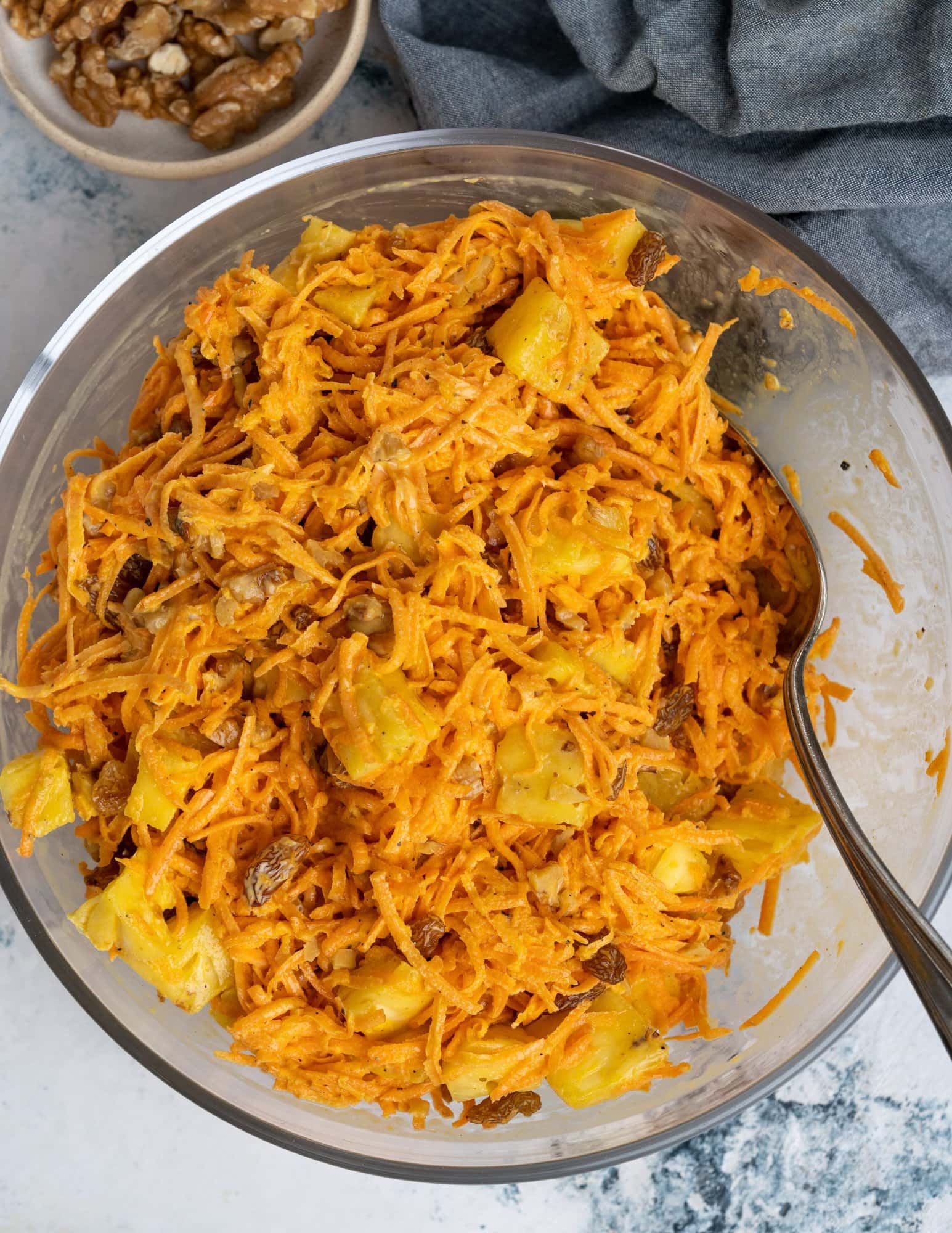 Carrot salad made of carrots, raisins, chopped pineapple and walnuts with a mayo-based creamy dressing, in a large bowl