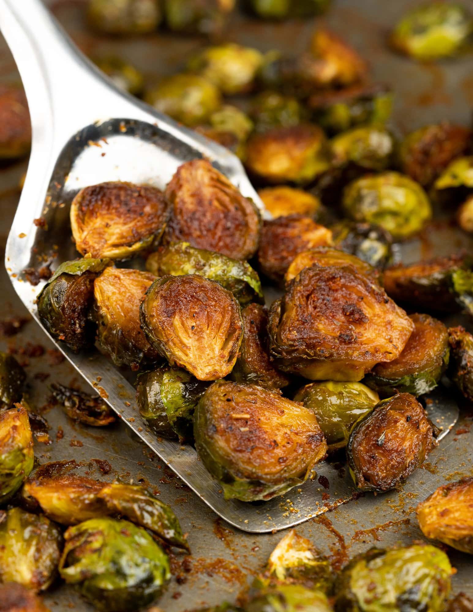 Oven roasted brussels sprouts appear caramelized with a golden crust and picked with a spatula.